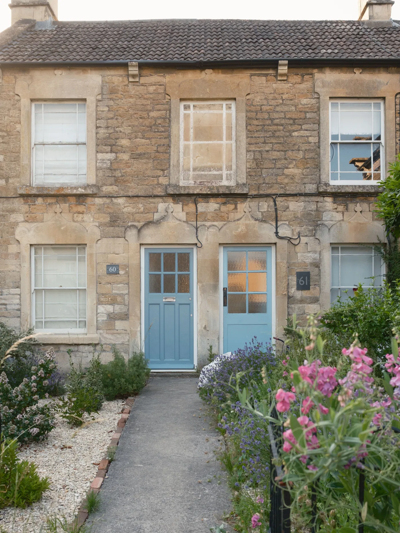A stone-fronted terraced home with a blue door, a front path and flowers.